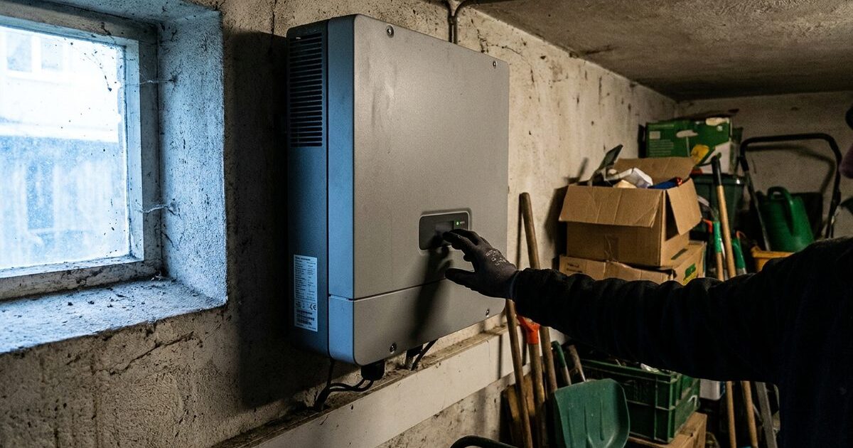Mano guantata che tocca il tasto di un inverter fotovoltaico appeso al muro di un garage