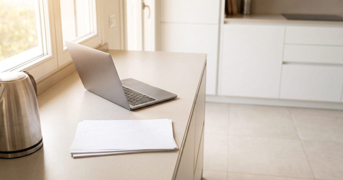 Laptop aperto e fogli di bolletta su un piano da cucina in un appartamento italiano illuminato dalla luce del giorno